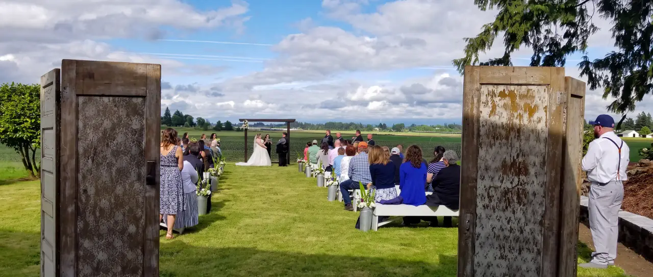 Beautiful outdoor wedding ceremony setup in an open field, featuring rustic wooden doors as the altar backdrop